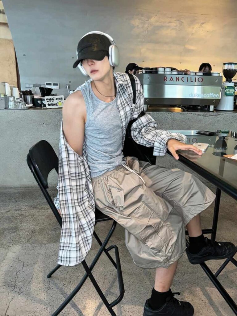 Matte cap + Over-ear headphones + Plaid overshirt + Athletic grey tank + Taupe tech-cargo capris + Black mesh trainers